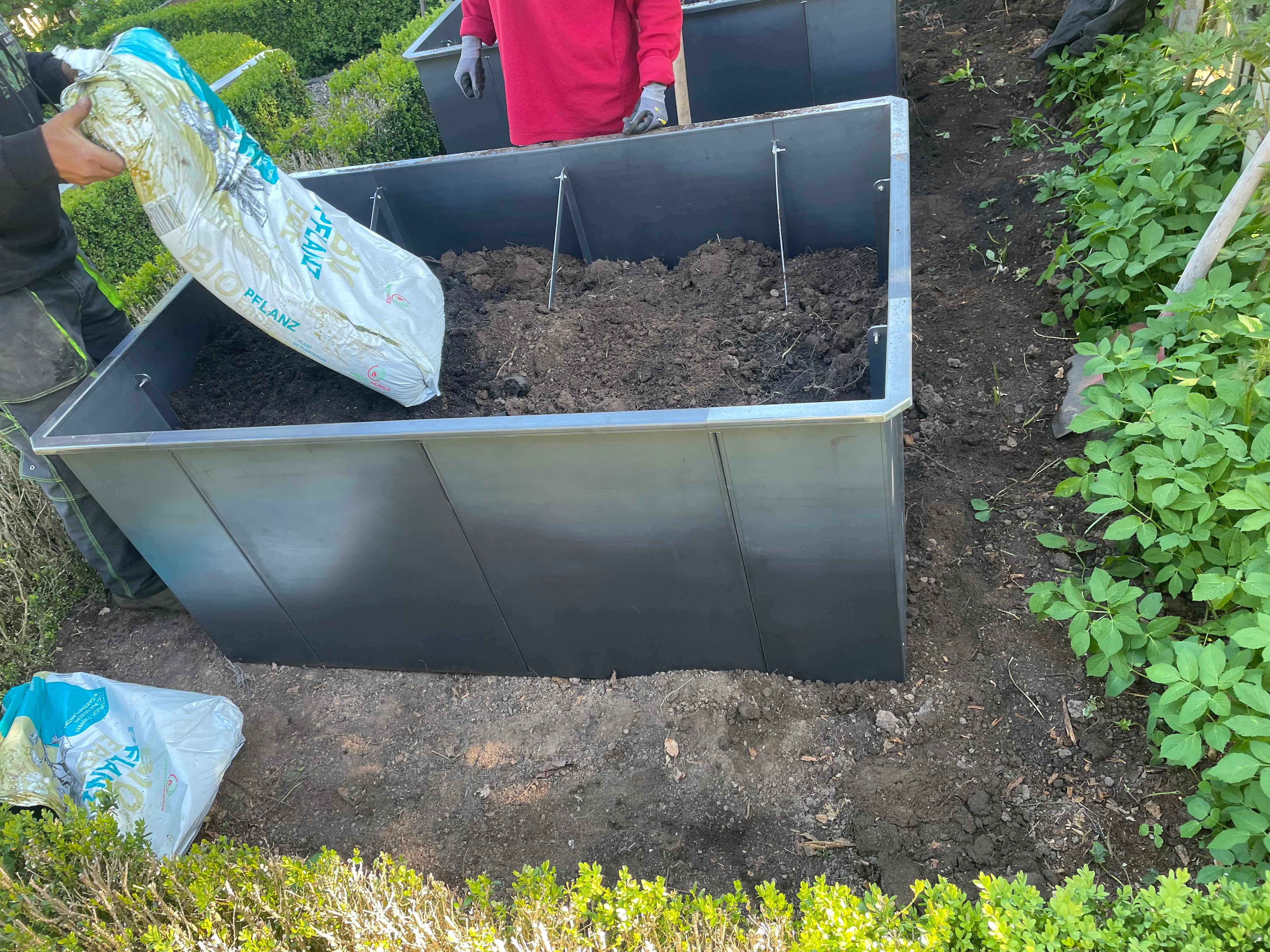 Personen befüllen ein Hochbeet aus Metall mit Erde