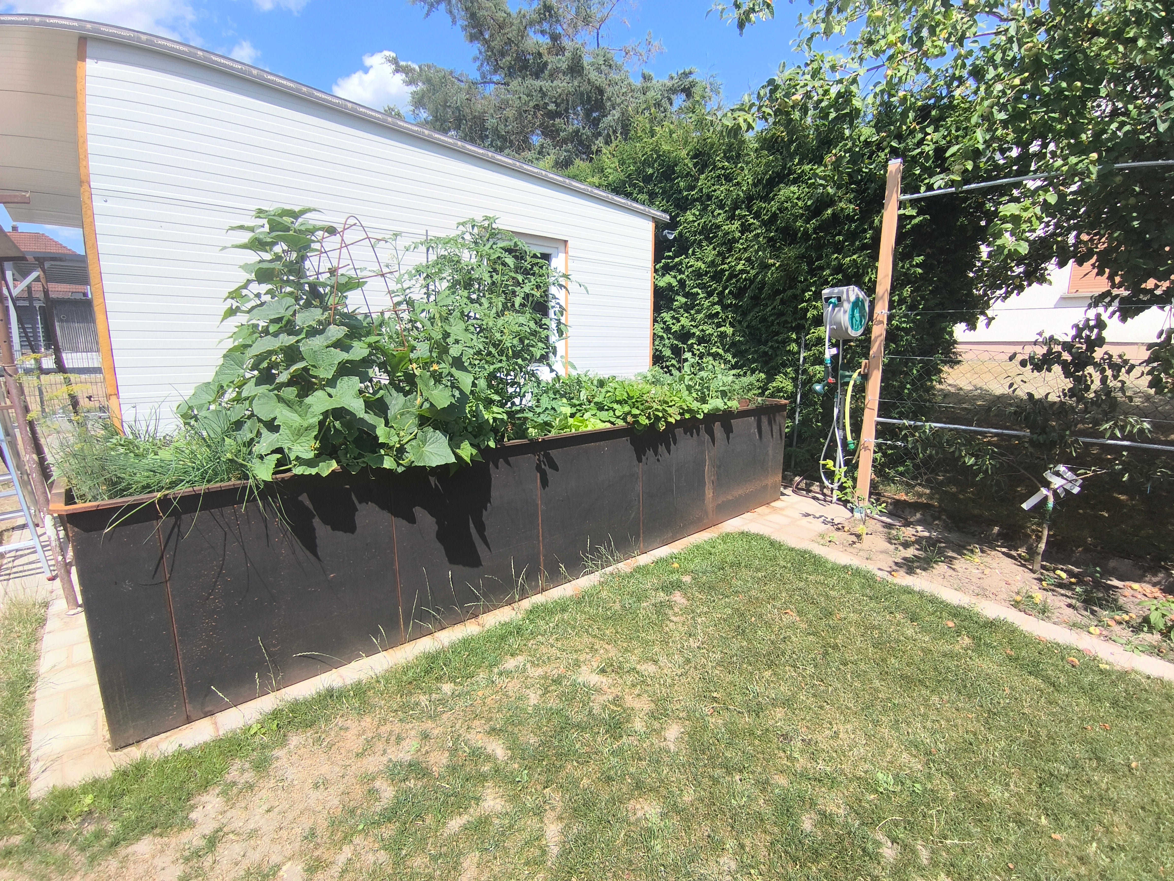 Bepflanztes Hochbeet aus Metall neben Gartenhaus