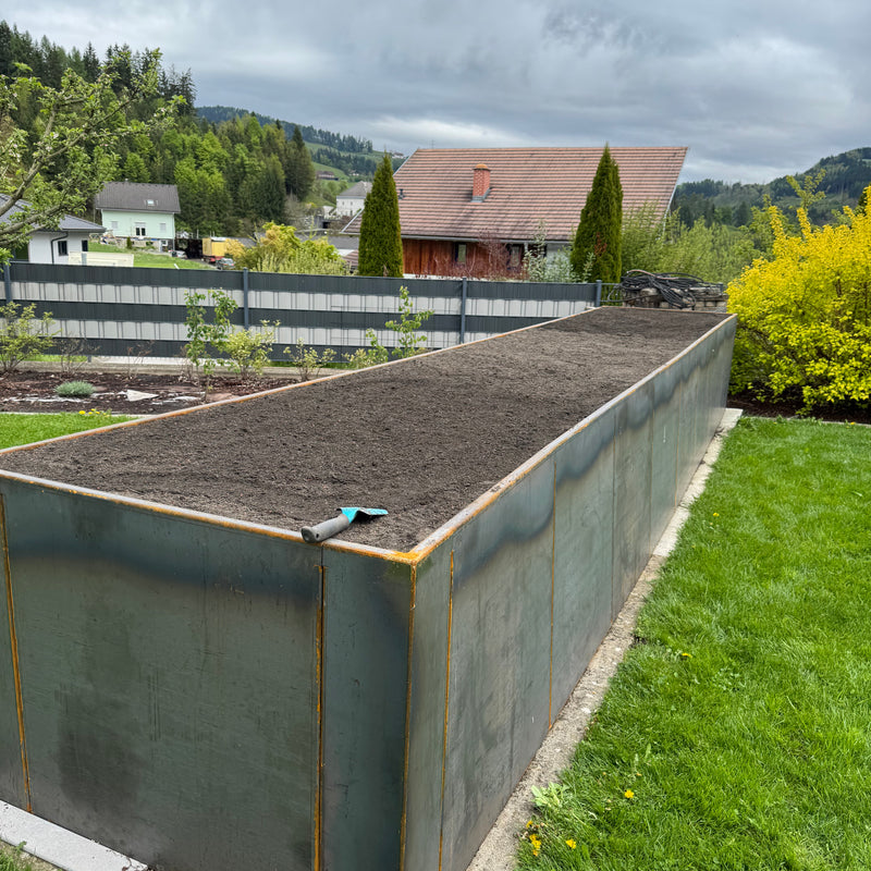 Großes Hochbeet aus Metall mit Erde im Garten